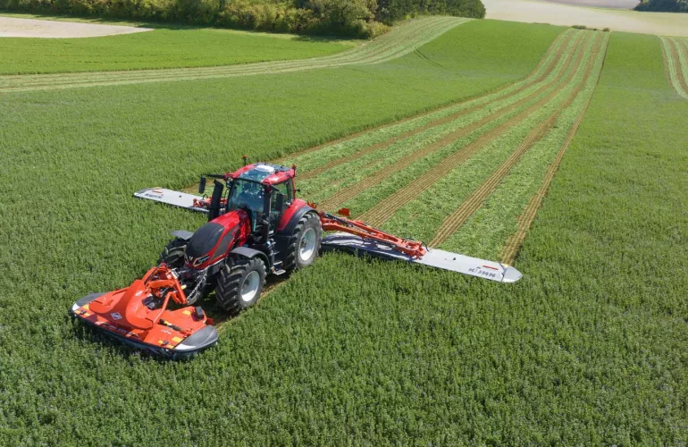 Vue sur la faucheuse agricole GMD 15030 tracté par tracteur VALTRA en plein travaux de fauchage en champs.