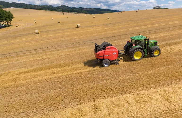 Vue d'ensemble d'une presse VB 7190 dans un champ de paille avec des balles rondes sous un beau ciel