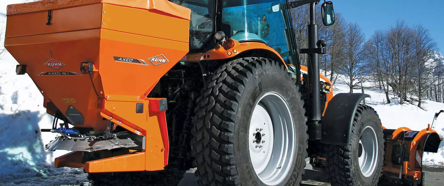 Distributeur AXEO de sel, sable, gravillons, engrais en action sur la route en montagne dans la neige avec skieur