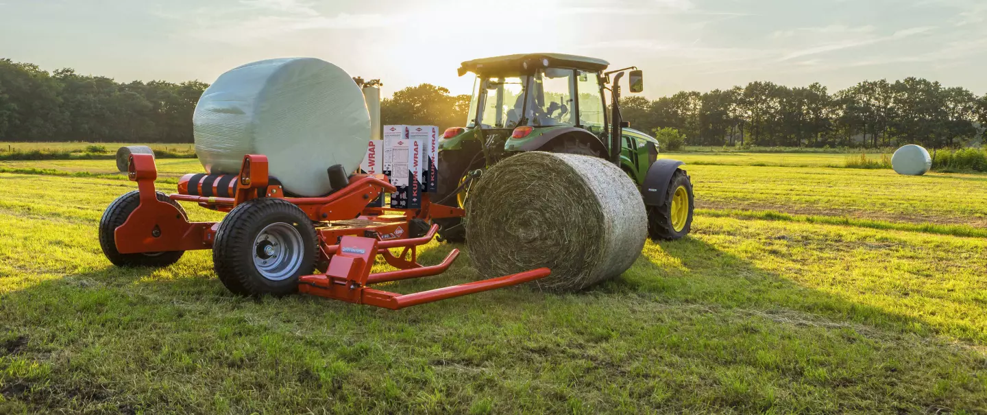 Enrubanneuse auto-chargeuse traînée pour balles rondes RW 1610 chargeant une balle ronde pendant l'enrubannage d'une autre balle.