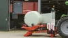 RW 1110 enrubannant une balle ronde devant une étable avec un robot d'alimentation en arrière-plan.